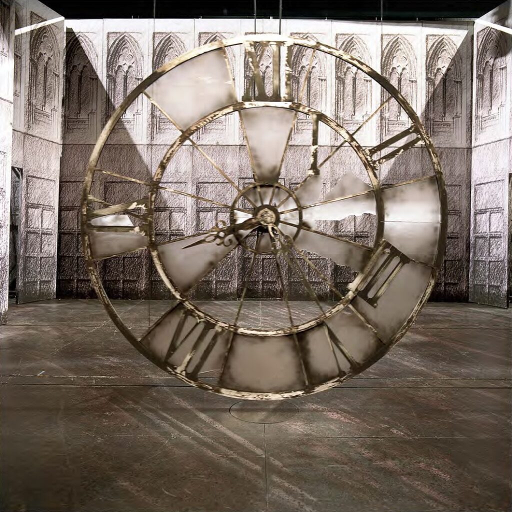 Décors d'opéra représentant une très grande horloge et en fond des sculptures nichées dans un mur - Agrandir l'image, fenêtre modale