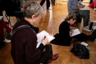 Des participants dessinent assis sur la parquet d'une salle du musée ou sur des chaises - Enlarge image 5 on 6, modal window