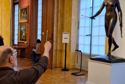 Un homme assis pointe son crayon vers une sculpture, comme pour estimer ses proportions. Il s'agit d'une sculpture assez imposante de la déesse Diane posée sur un socle. Diane est représentée nue, avec une flèche dans la main droite et son arc dans la main gauche. - Enlarge image 4 on 6, modal window