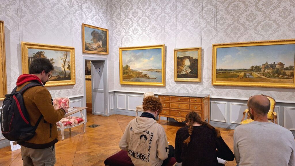 3 personnes assises + 1 debout observent les peintures - paysages de l'époque Transition - et les croquent - Agrandir l'image, fenêtre modale